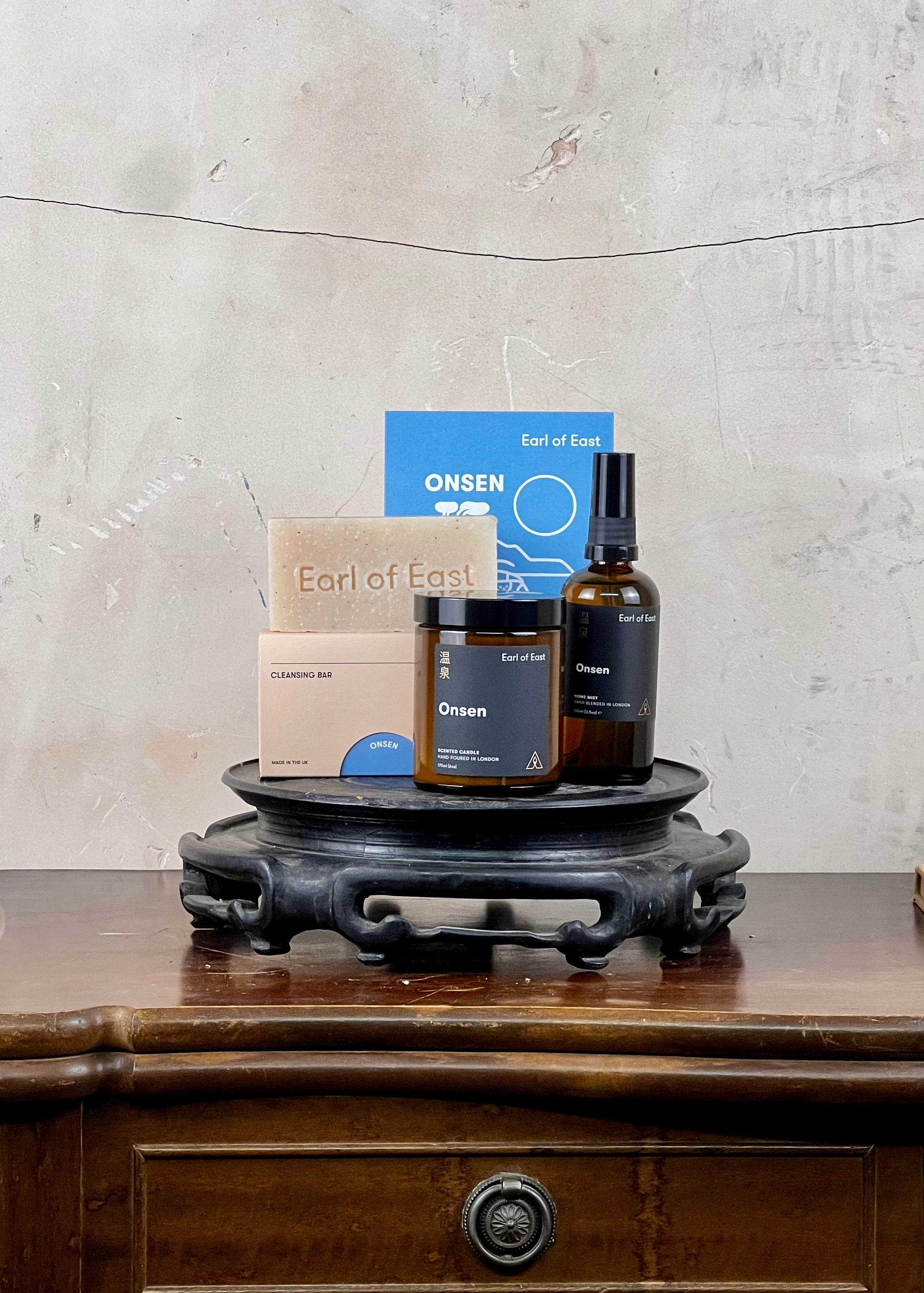 Cosmetic products from Earl of East on a wooden stand with a textured wall background