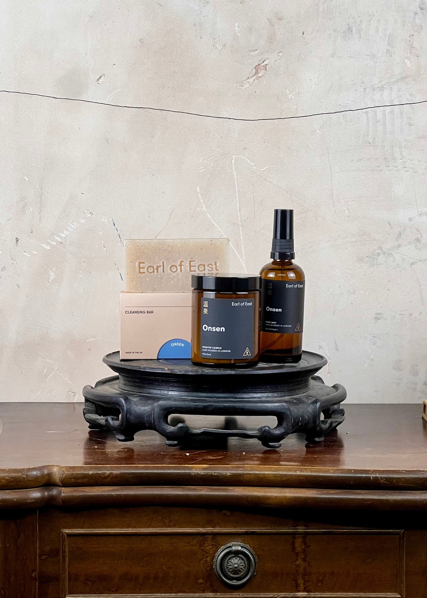 Skincare products  from Earl of East and a candle on a wooden stand with a textured wall background