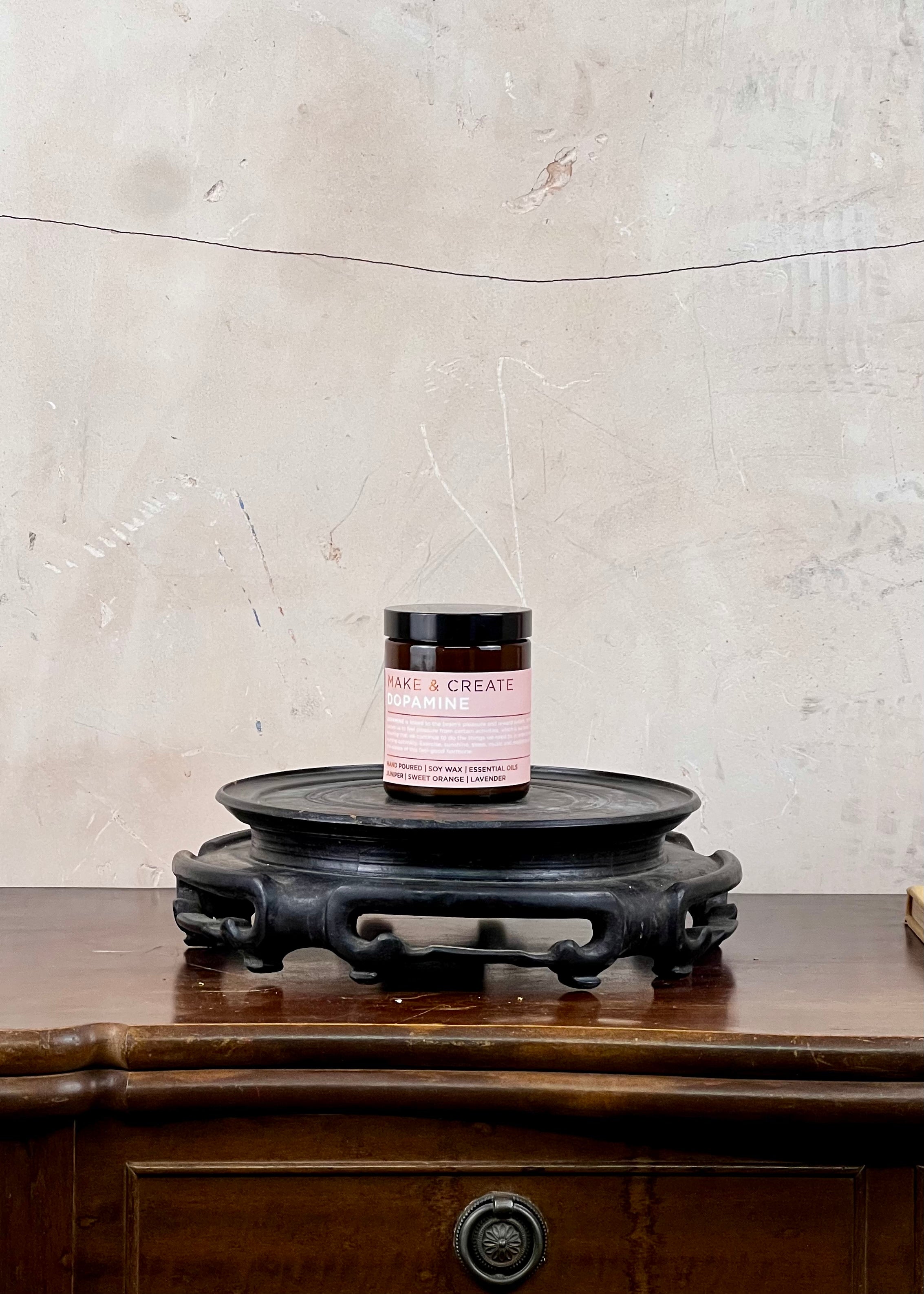 A soy wax candle jar on a wooden surface with a textured wall background