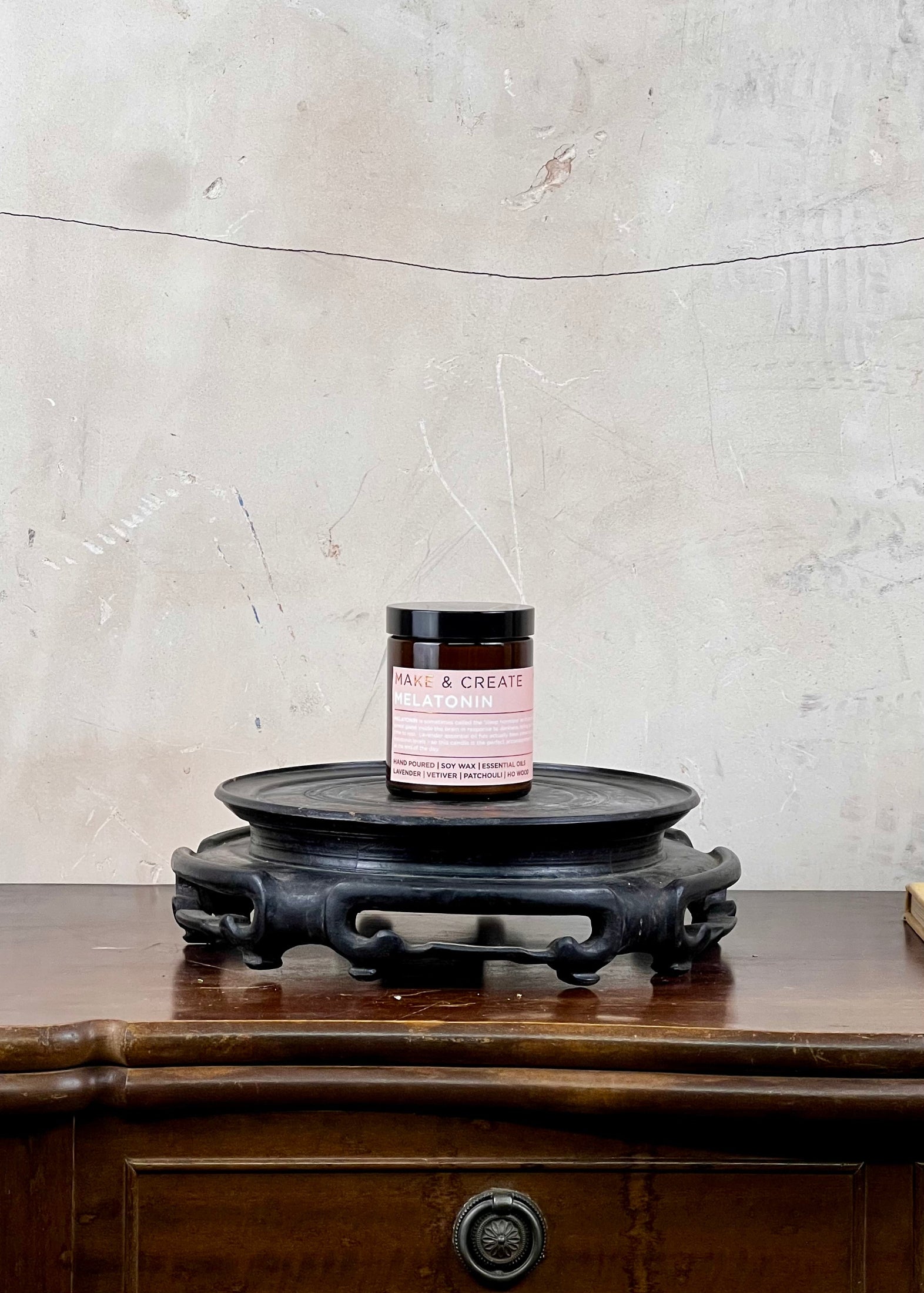 A soy wax candle jar on a wooden surface with a textured wall background