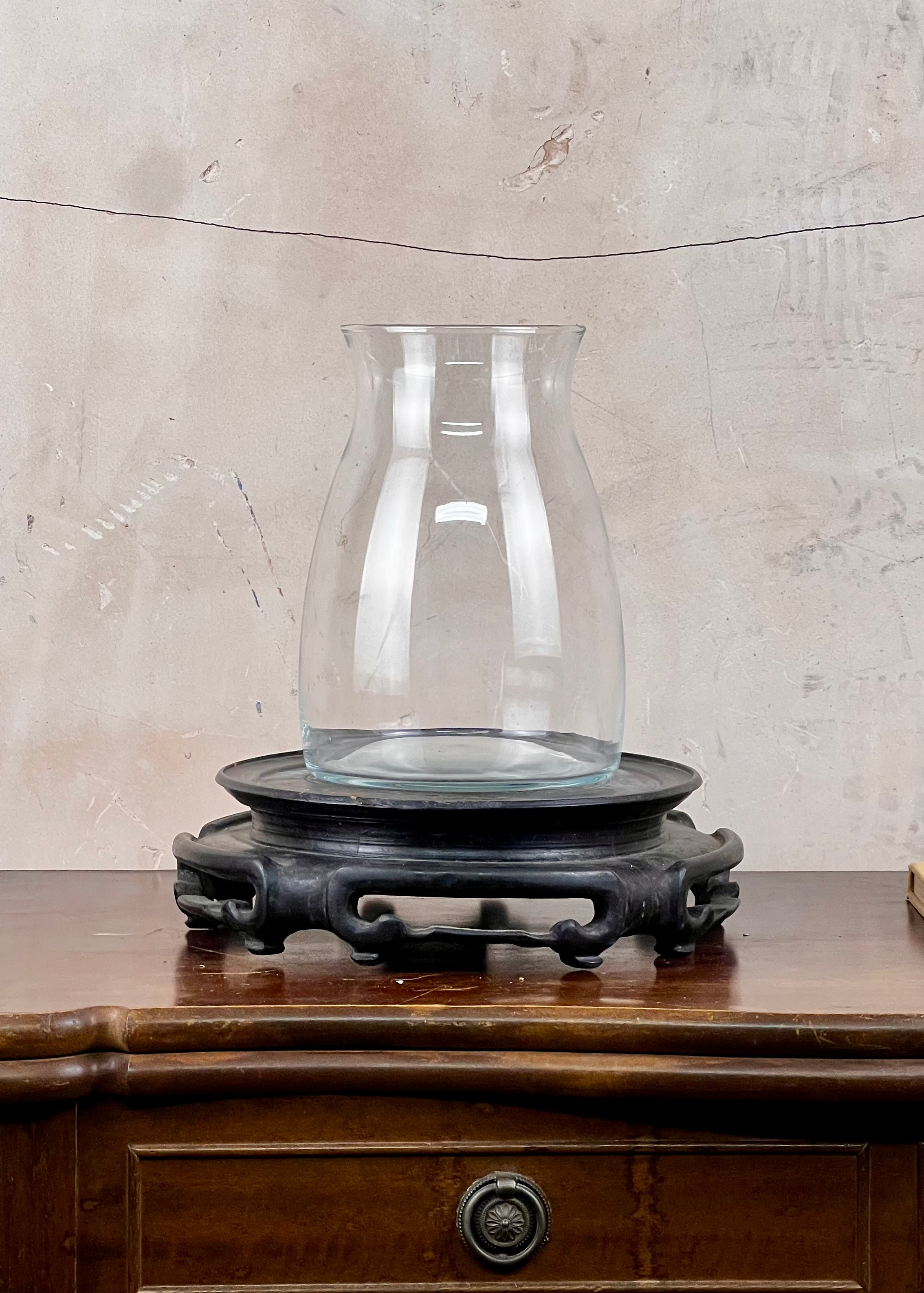 Clear glass vase on a wooden stand against a textured wall.