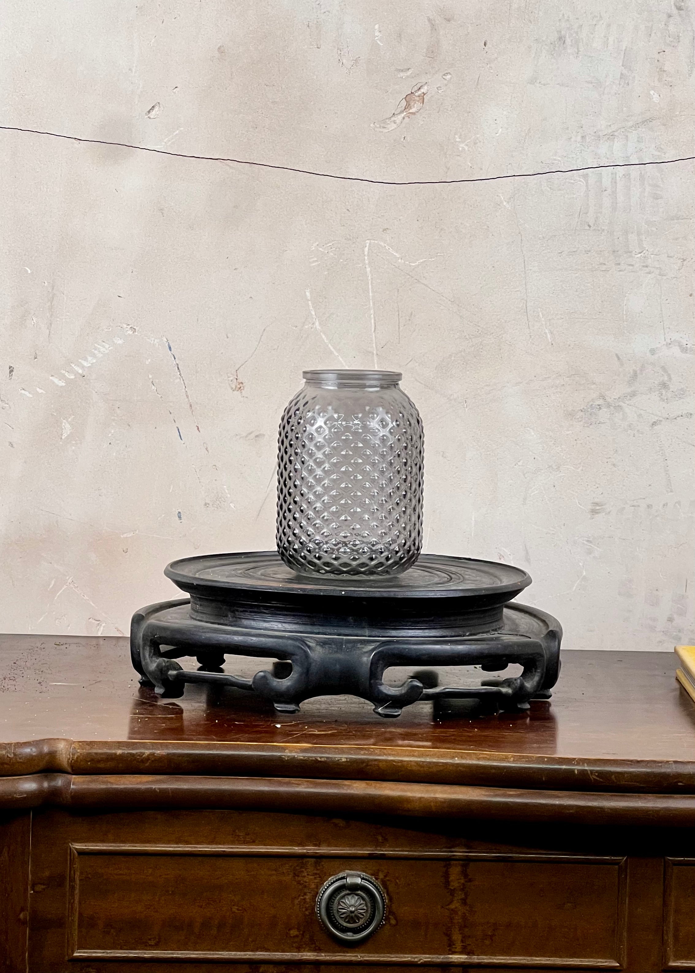 Decorative glass jar on a wooden stand against a textured wall.